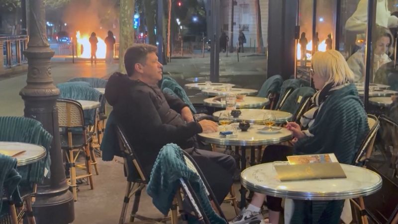 A couple enjoys a drink on the fringe of Paris rioting